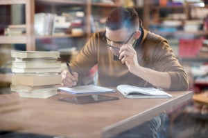 Nerdy college student studying for his exams in library.